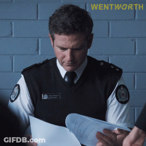 A Police Officer Is Looking At A Piece Of Paper With Wentworth Written On The Bottom GIF