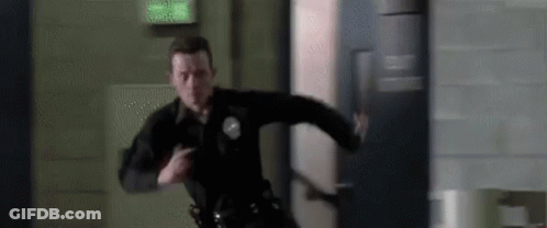 A Police Officer Is Running Through A Hallway With A Gun In His Hand . GIF
