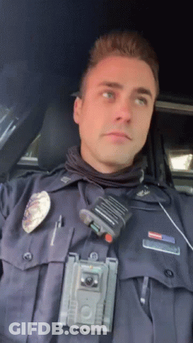 A Police Officer Is Sitting In A Car With A Walkie Talkie On His Chest GIF