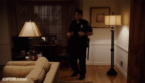 A Police Officer Is Standing In A Living Room Holding A Cup GIF