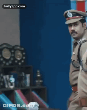 A Police Officer Is Standing In A Room With A Lot Of Trophies On The Shelf . GIF
