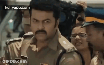 A Police Officer Is Standing In Front Of A Crowd Of People . GIF