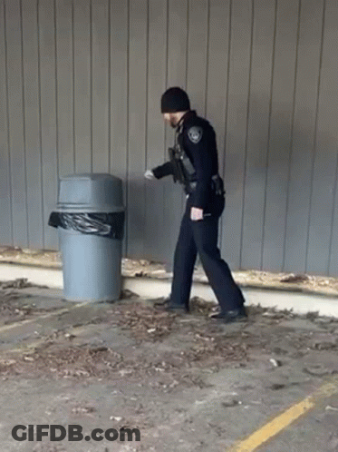 A Police Officer Is Walking Towards A Trash Can . GIF