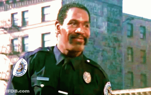 A Police Officer Stands In Front Of A Building With The Letter F On The Side GIF