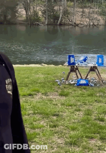 A Police Officer Stands In Front Of A Lake With A Few Coolers On The Ground GIF