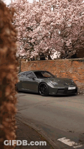 A Porsche Sports Car Is Parked In Front Of A Brick Wall GIF