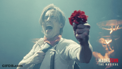 A Poster For Hadestown The Musical Shows A Man Holding A Red Flower In His Hand GIF