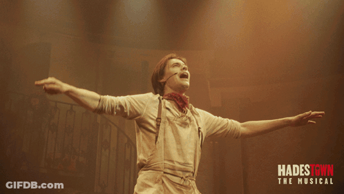 A Poster For Hadestown The Musical With A Man Holding A Red Flower GIF