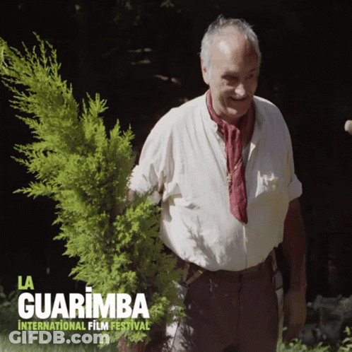 A Poster For La Guarimba International Film Festival Shows A Man Holding A Small Tree GIF