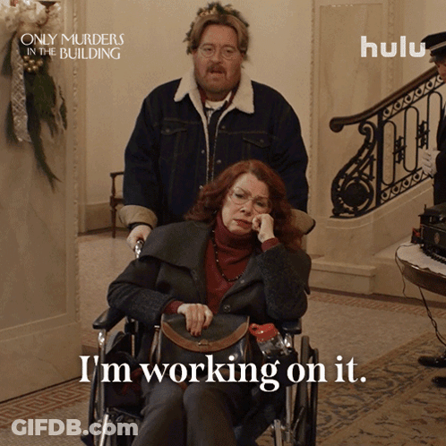 A Poster For Only Murders In The Building Shows A Woman In A Wheelchair And Says I 'M Working On It GIF