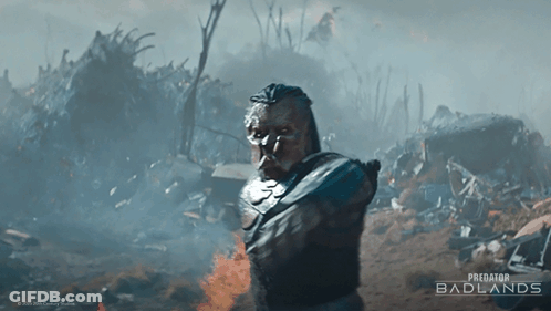 A Poster For Predator Badlands Shows A Man Standing In A Pile Of Trash GIF