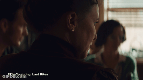A Poster For The Conjuring Last Rites Shows A Woman Sitting At A Table GIF