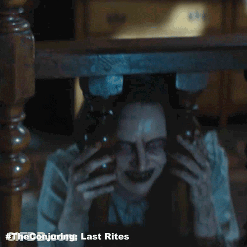 A Poster For The Conjuring Last Rites With A Scary Woman Behind A Table GIF