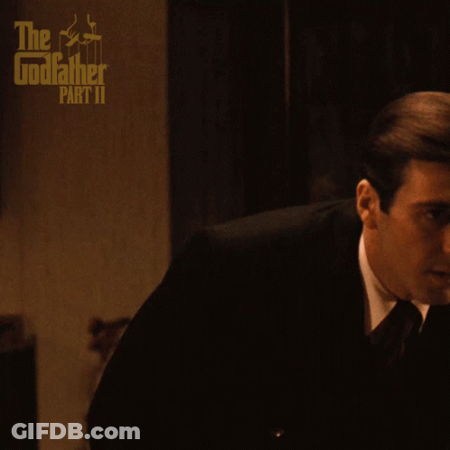 A Poster For The Godfather Part Ii Shows A Man In A Suit And Tie Sitting On A Couch GIF