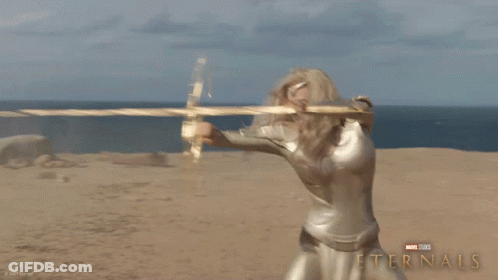 A Poster For The Movie Eternals Shows A Blonde Woman Holding A Golden Object GIF