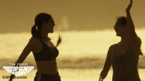A Poster For Top Gun Maverick Shows Two Women Dancing On The Beach GIF