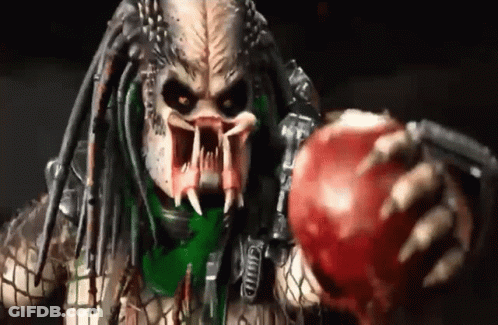 A Predator Is Holding A Red Apple With His Mouth Open . GIF