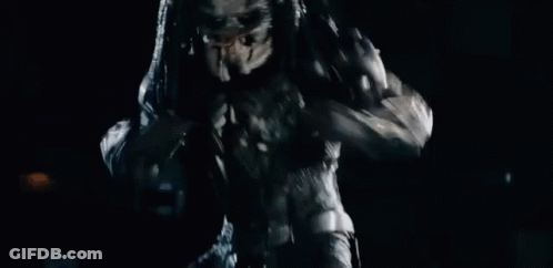 A Predator Is Standing In The Dark With Its Arms Outstretched And Looking At The Camera . GIF