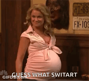 A Pregnant Woman In A Pink Shirt Is Standing In Front Of A Sign That Says Guess What Switart . GIF