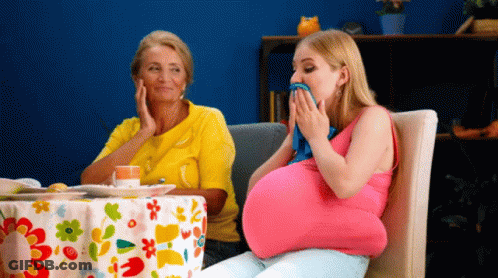 A Pregnant Woman Is Sitting At A Table With A Floral Tablecloth GIF