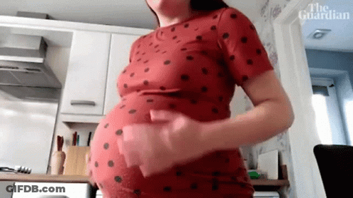 A Pregnant Woman Is Standing In A Kitchen Holding Her Belly . GIF