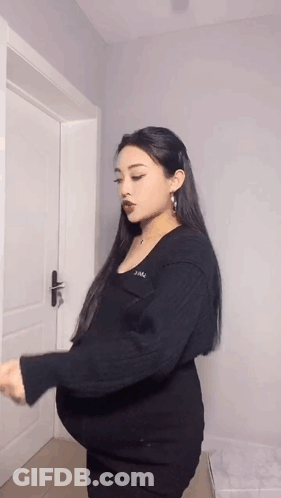 A Pregnant Woman Is Standing In Front Of A Door Holding Her Belly . GIF
