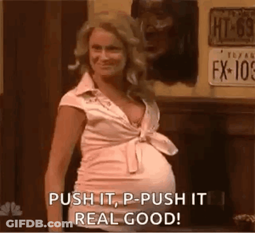 A Pregnant Woman Is Standing In Front Of A Sign That Says Push It , P - Push It Real Good . GIF