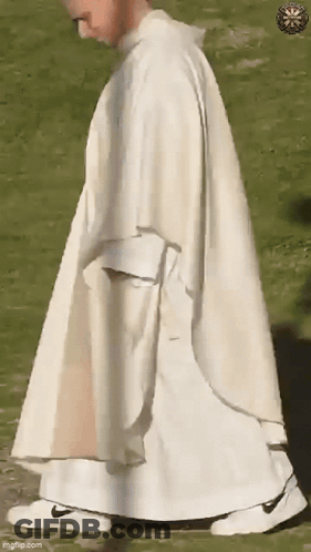 A Priest In A White Robe And White Sneakers Is Walking In A Field . GIF