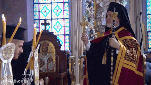 A Priest Is Holding A Cross In Front Of A Stained Glass Window In A Church GIF