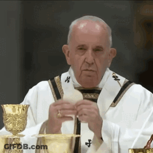 A Priest Is Holding A Piece Of Bread In Front Of A Chalice GIF