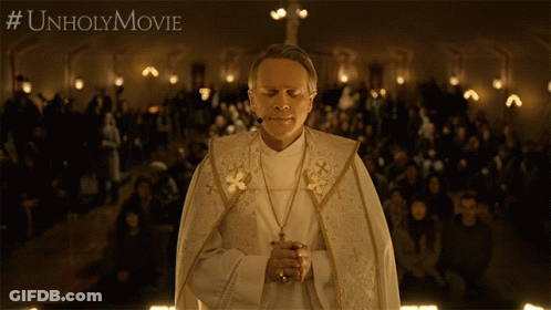 A Priest Is Praying In Front Of A Crowd With #Unholymovie Written On The Bottom Right GIF