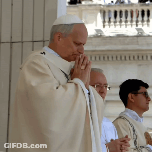A Priest Is Praying With His Hands Folded In Front Of A Balcony GIF