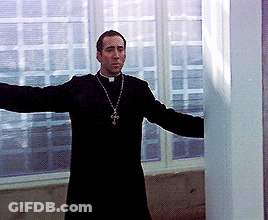 A Priest With His Arms Outstretched And A Cross On His Neck GIF