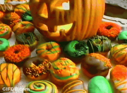 A Pumpkin With A Face Carved Into It Sits On Top Of A Pile Of Donuts GIF
