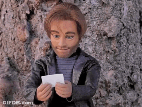 A Puppet Is Leaning Against A Tree And Holding A Piece Of Paper GIF