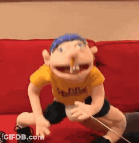 A Puppet Is Sitting On A Red Couch With A Stick In His Mouth . GIF