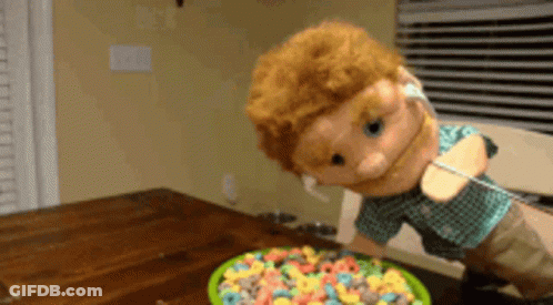 A Puppet Is Standing Next To A Bowl Of Fruit Loops GIF
