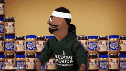 A Puppet Wearing A Green Shirt That Says Feeding America Stands In Front Of Jars Of Peanut Butter GIF