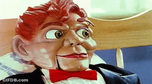 A Puppet Wearing A Tuxedo And Bow Tie Is Sitting On A Chair . GIF