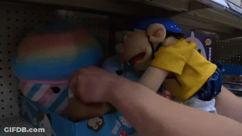 A Puppet With A Pencil In His Mouth Is Sitting On A Shelf In A Store .. GIF