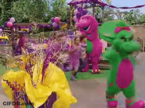 A Purple And Green Dinosaur Standing Next To A Yellow Flower GIF