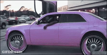 A Purple Car With Big Wheels Is Parked In A Lot GIF
