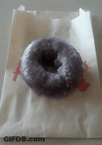 A Purple Donut Is Sitting On A White Paper Bag With The Letter A Printed On It GIF