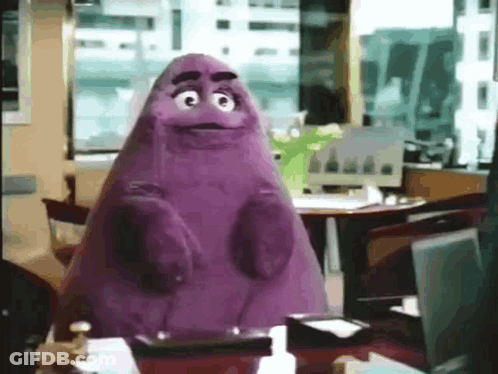 A Purple Mcdonald 'S Mascot Is Sitting At A Desk In An Office . GIF