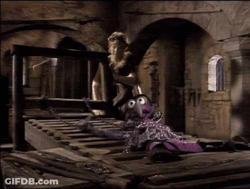 A Purple Puppet Is Chained To A Wooden Railing GIF