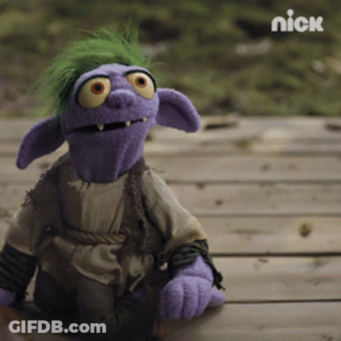 A Purple Puppet With Green Hair And Orange Eyes Is Sitting On A Wooden Surface With The Nick Logo In The Background GIF