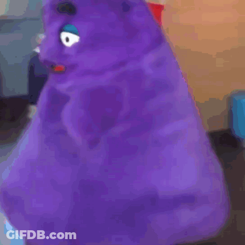 A Purple Stuffed Animal With A Blue Eye Is Sitting In A Room . GIF