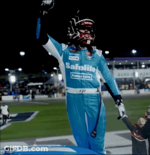 A Race Car Driver Wearing A Blue Safelite Uniform Stands On The Hood Of His Car GIF
