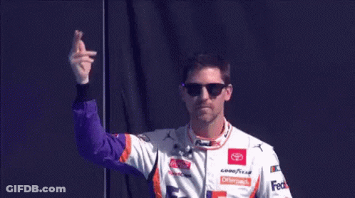 A Race Car Driver Wearing Sunglasses And A Fedex Shirt Is Waving His Hand . GIF