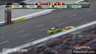 A Race Car Is Driving Down A Race Track With A Scoreboard Behind It . GIF